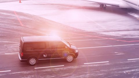 Black VIP service van running on airport taxiway with blurred private jet on background. Business class service at airport. Security intelligence agency hurrying at airfield. toned